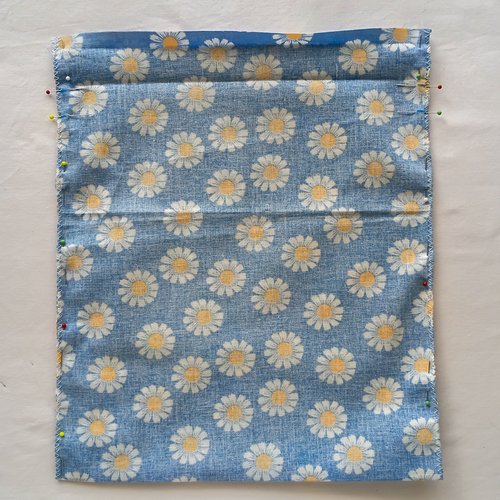 Two pieces of blue daisy fabric pinned together along the side edges with colorful sewing pins.