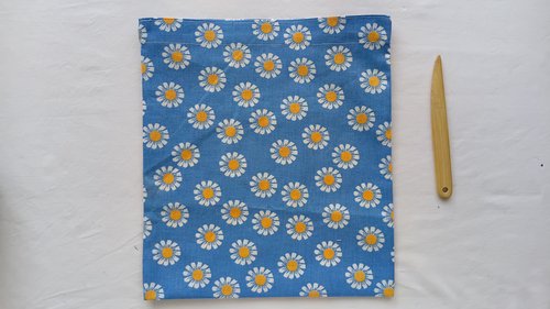 A finished blue daisy bag turned right-side out, sitting next to a wooden turning tool.
