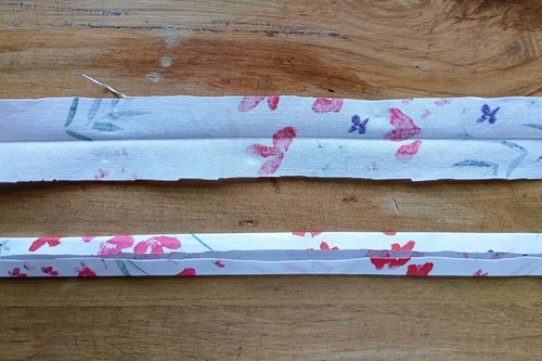 A close-up of a long, thin strip of floral fabric with a crease in the center, and below a strip of floral fabric folded into the center crease.