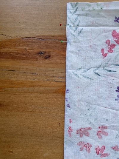 A close-up of the edge of a floral fabric turned inside out and held together with sewing pins.