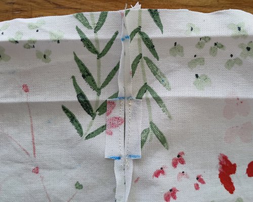 A close-up of a vertical seam pressed flat open on the floral fabric, with stitching outlining a small rectangular gap in the middle.