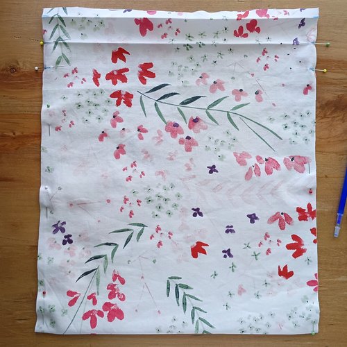 A piece of floral fabric folded at the top and held together with sewing pins along the side edges.
