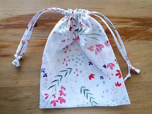 A floral fabric bag laid flat, with two drawstrings sticking out from the top sides.