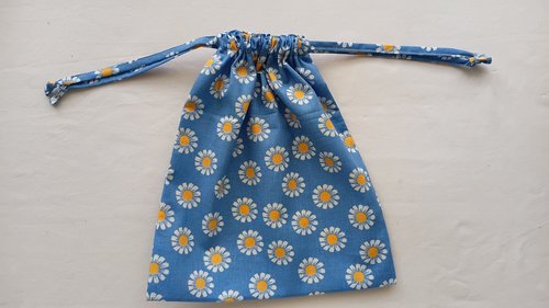 A drawstring bag made of blue fabric with white and yellow daisies