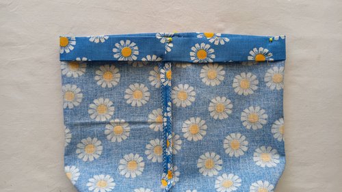 A top edge of a blue floral fabric bag folded over toward the inside of the bag and pinned
