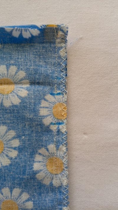 A side seam of a blue floral bag sewn with white thread, leaving a small gap in the stitching.