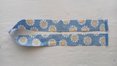 A short end of a blue floral fabric strip folded over and sewn with a straight stitch.