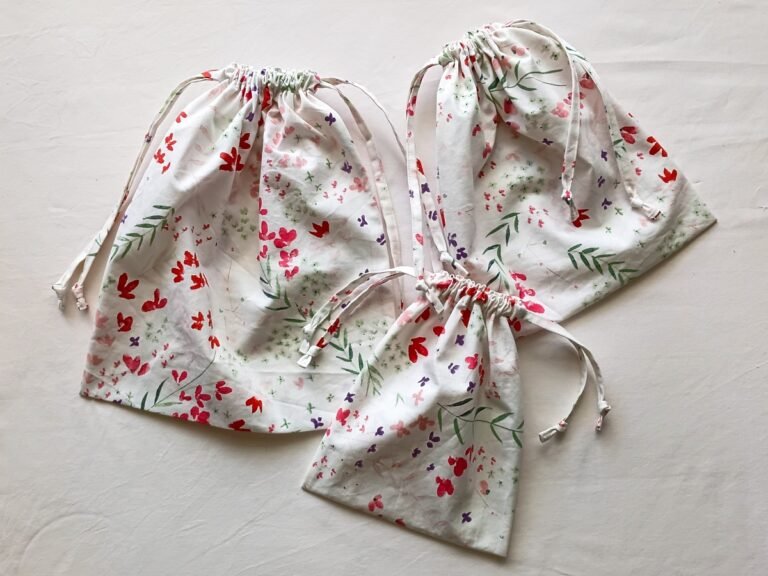 Three floral drawstring bags in small, medium, and large sizes, all gathered at the top and arranged on a light neutral background.
