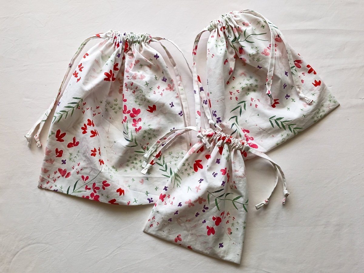 Three floral drawstring bags in small, medium, and large sizes, all gathered at the top and arranged on a light neutral background.