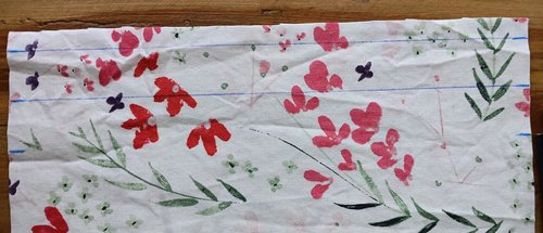 A close-up of white fabric with a pink and green floral pattern, featuring straight blue lines drawn across the top section.