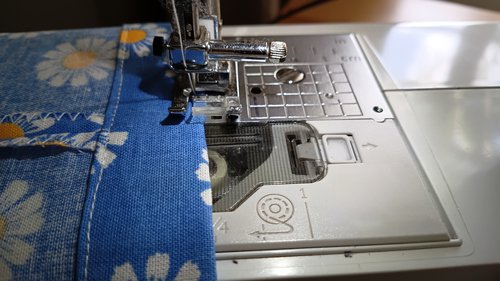 A close-up of a side opening on a blue floral bag with white topstitching around the edges.