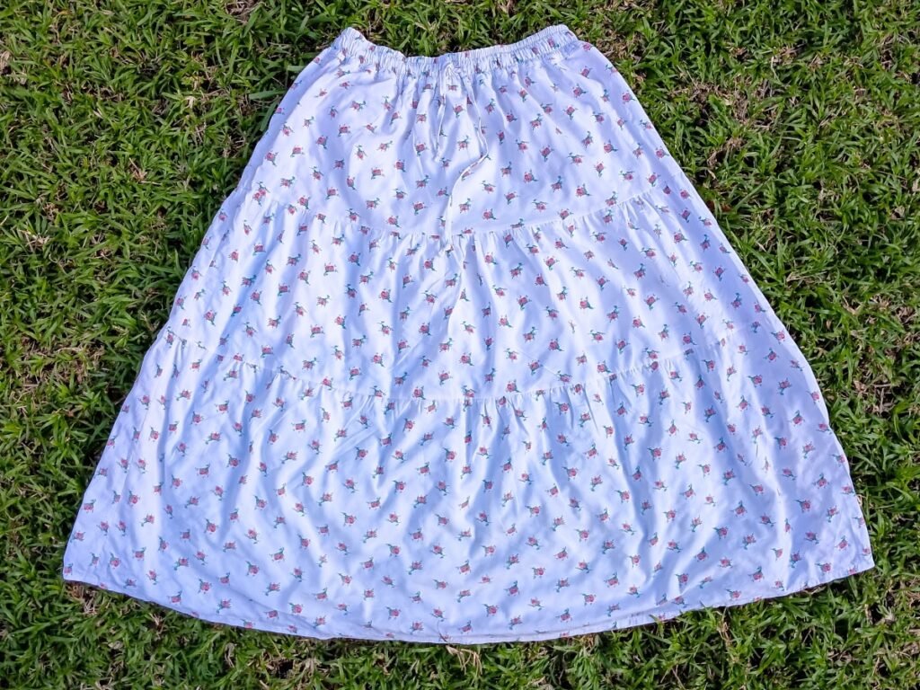 A white, three-tiered floral maxi skirt laid flat on green grass.