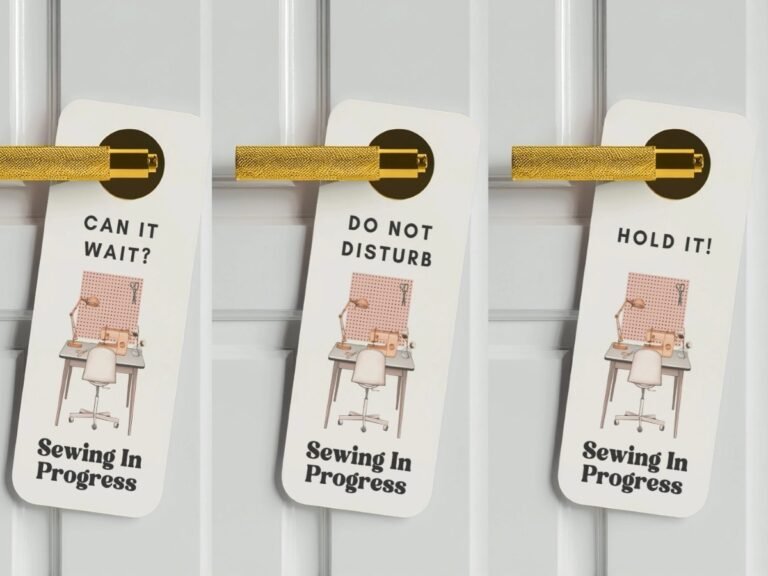 Three white door hangers with gold handles, each showing a sewing workspace illustration and the words “Sewing In Progress,” with different messages at the top: “Can It Wait?”, “Do Not Disturb,” and “Hold It!”