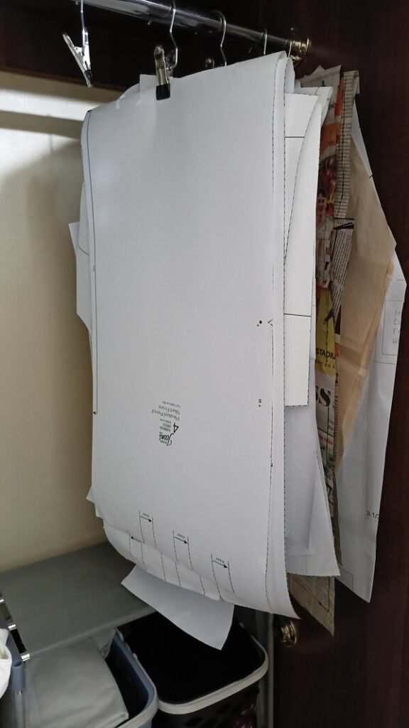 Sewing pattern pieces hanging from a closet rail, with a large white skirt front pattern piece clipped to a hanger.