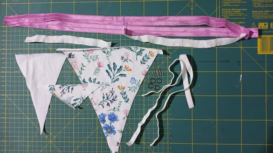 Sewing supplies for the Nyuzi G-string pattern, including cut fabric pieces, fold-over elastic, bra strap elastic, sliders, and rings.