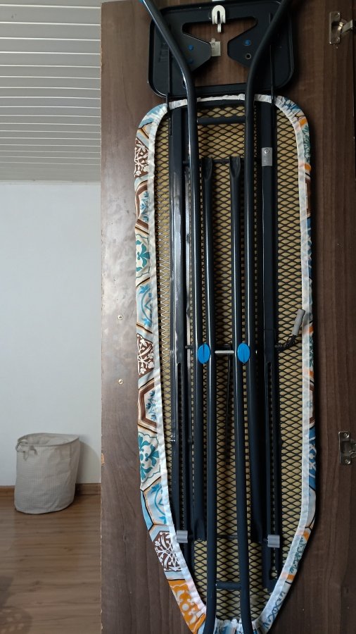 Folded ironing board stored vertically on the inside of a wardrobe door to save space in the sewing area.