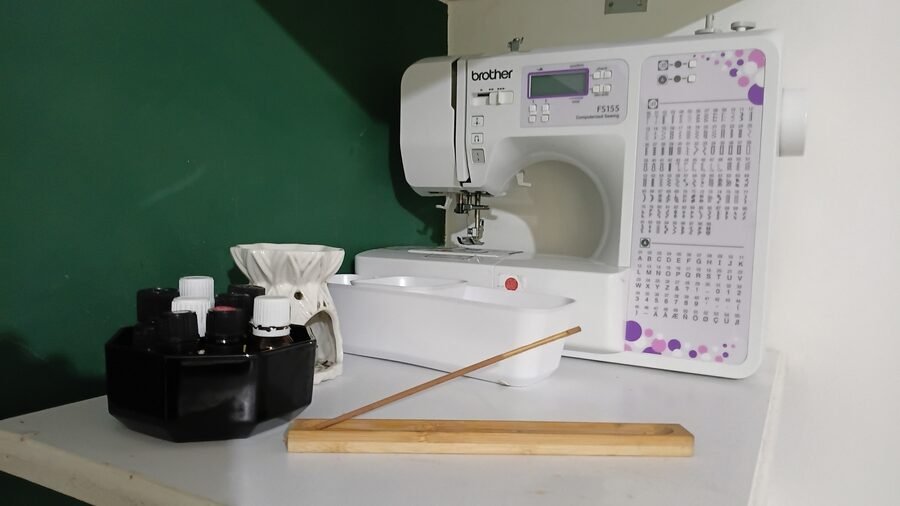 Close-up of a sewing machine on a wall-mounted shelf, with small containers and essential oils and an incense stick and essential oil burner.