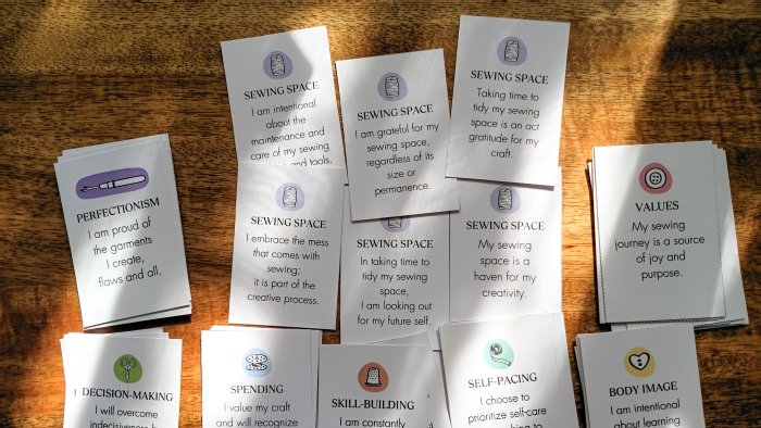 Collection of sewing affirmation cards spread across a table, featuring positive messages about creativity, organization, skill-building, and confidence in sewing.