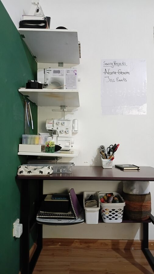 Front view of a compact sewing workstation featuring wall-mounted shelves with sewing machines, a worktable, and organized storage underneath.