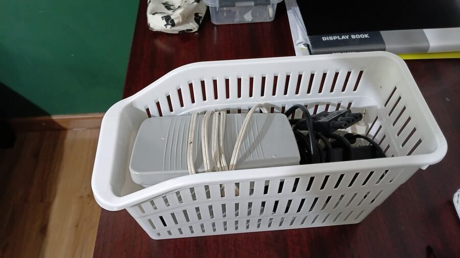 Basket containing sewing machine and serger foot pedals, power cords, and accessories stored on the worktable.