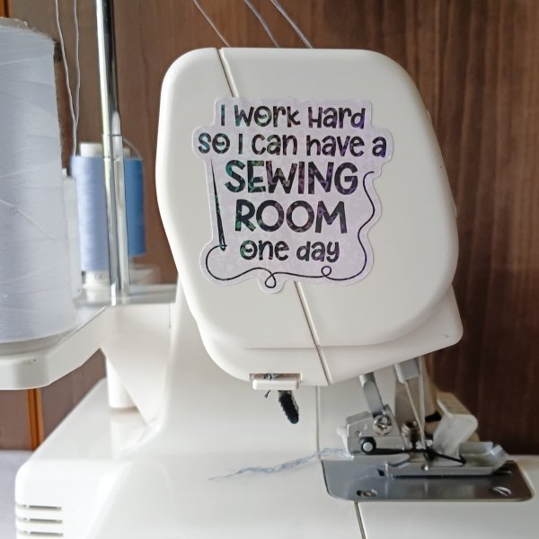 Close-up of a serger with a decorative sticker that reads, “I work hard so I can have a sewing room one day.”