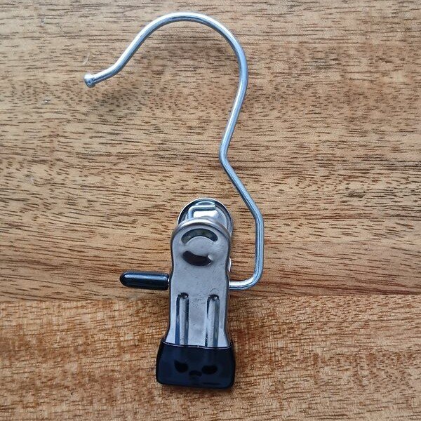Metal hanger clip with a black rubber tip on a wooden surface.