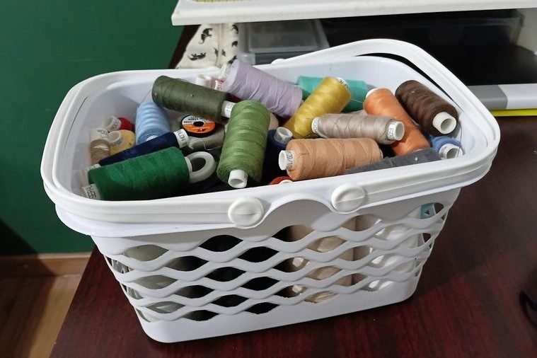 Plastic basket filled with thread spools in various colors for sewing and serging projects.