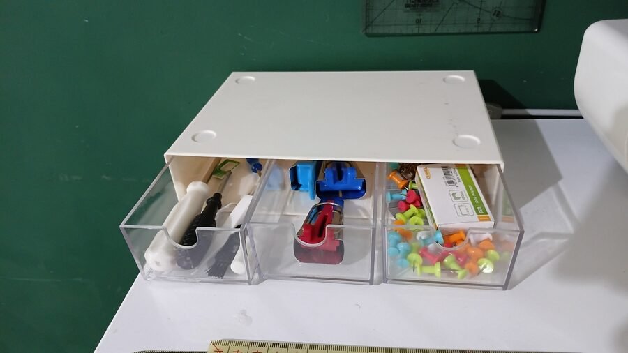 Small three-drawer organizer on a sewing shelf, holding clips, seam rippers, marking tools, and other sewing notions.