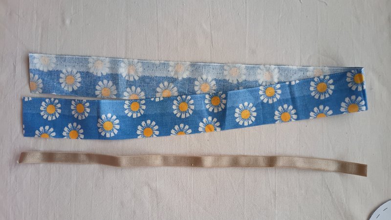 Daisy print fabric strip folded lengthwise beside a length of beige elastic.