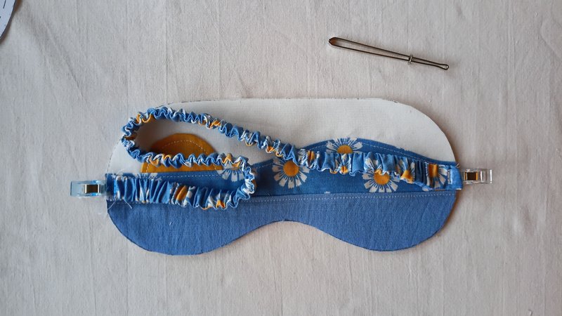 A fabric covered elastic strap clipped onto sleep mask front.