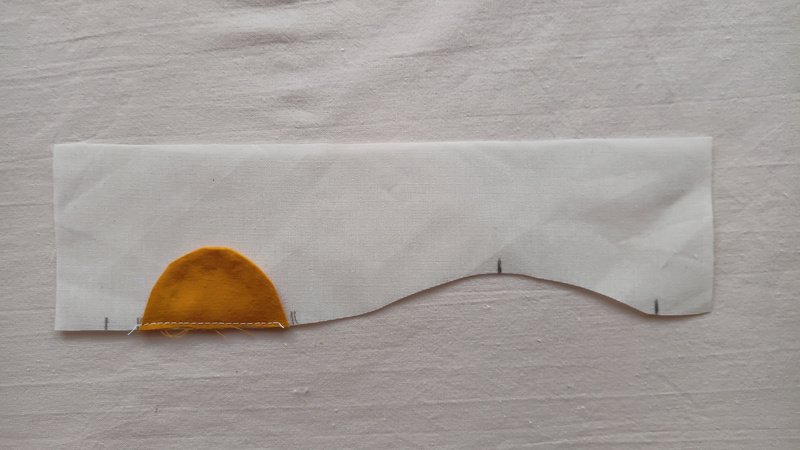 A yellow sun applique sewn onto a piece of off-white fabric