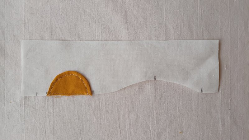 A top-stitched yellow sun applique sewn onto a piece of off-white fabric