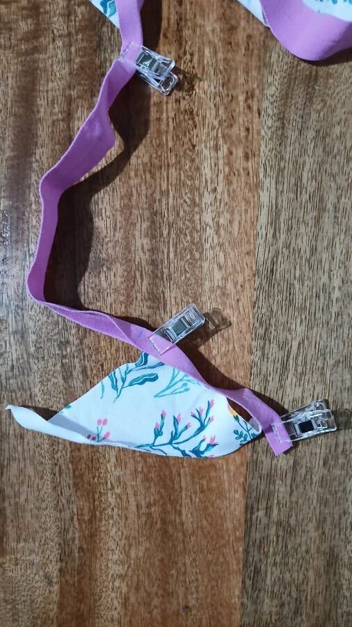 Triangular piece of floral fabric clipped to pink fold over elastic from the bottom