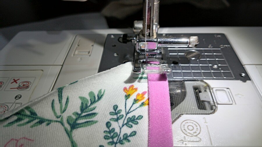 The throzt plate, shank and presser foot of a sewing machine with floral fabric enclosed by pink fold over elastic