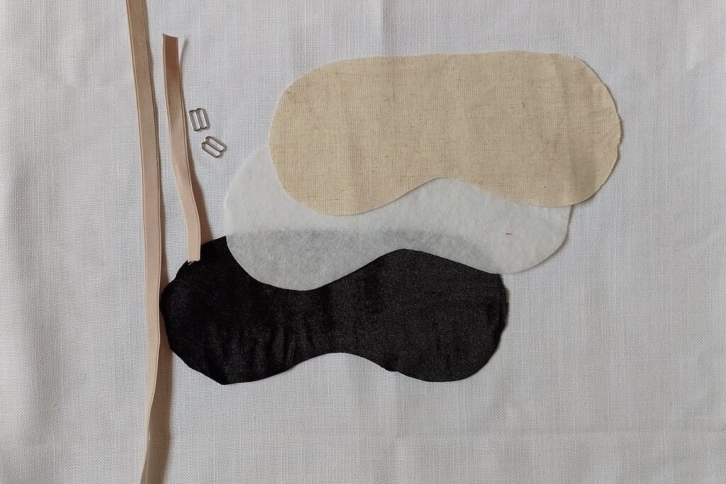 Beige bra elastic, two silver sliders. Blak velvet, fusible batting and beige linen cut out in the shape of a sleep mask template.