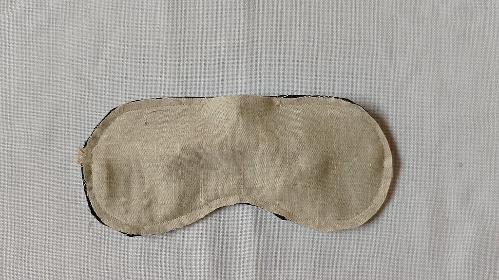 The back of a sleep mask that is inside out. It has a line of stitching and a gap at the top.