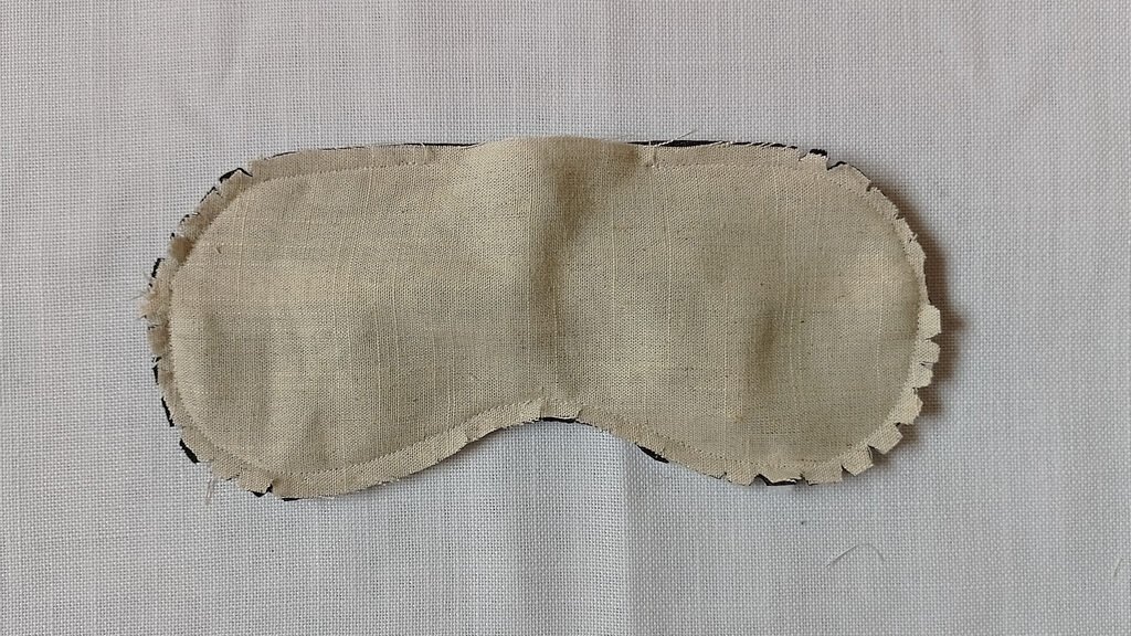 The back of a sleep mask. The mask has a gab that hasn't been sewn and is inside out. It also has been clipped at the seam allowance.