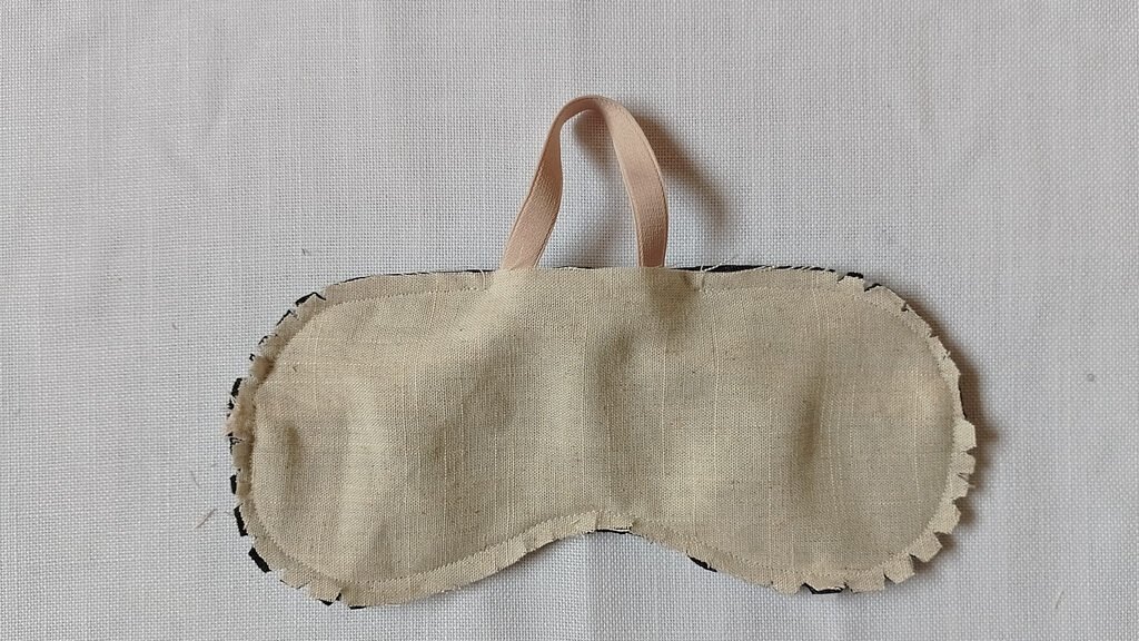 The back of a sleep mask with a beige strap coming out of a hole in the mask. The mask is inside out and has been clipped at the seam allowance.