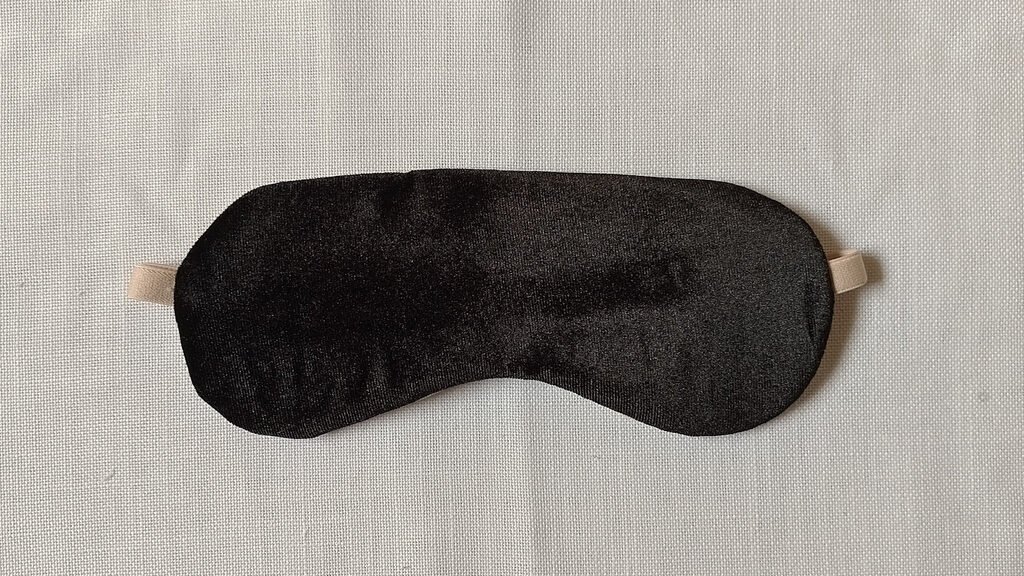 The front of a sleep mask. It has black velvet fabric and a beige adjustable strap