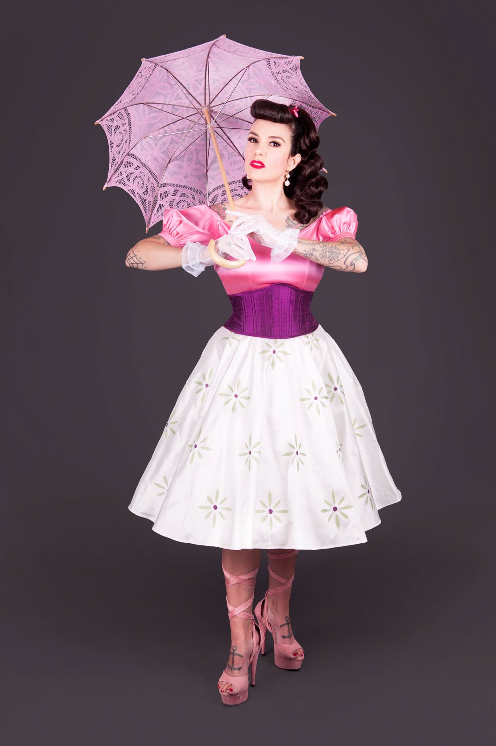 Woman in a pink satin puff-sleeve bodice, purple corset waist, and white daisy-print circle skirt holding a lilac parasol