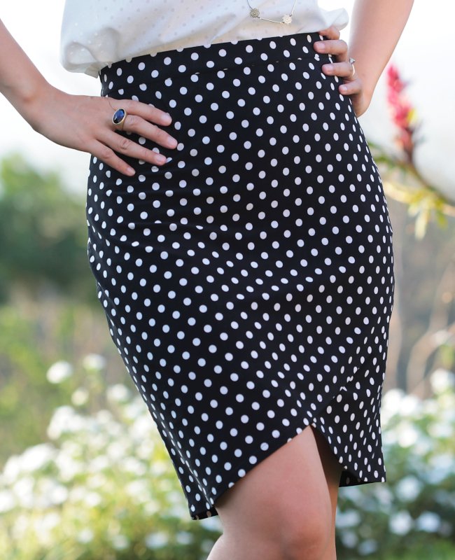 Woman in a black-and-white polka dot pencil skirt with a tulip hem, tucked hands on hips