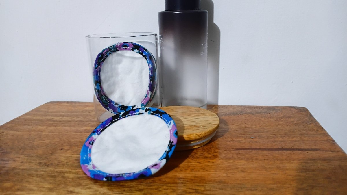 Two finished flannel rounds edged with floral bias tape, one standing in a glass jar and one resting on a wooden table