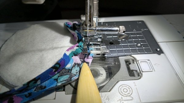Floral bias tape looped around a flannel round under the sewing machine needle