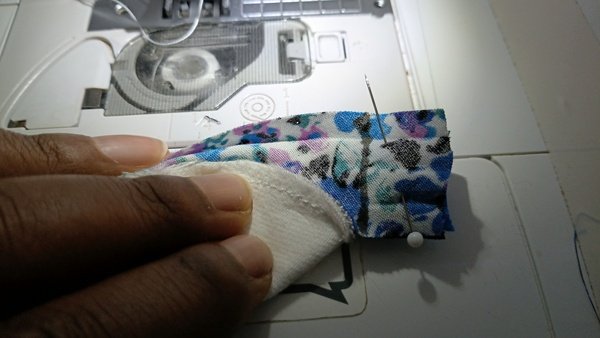 Hand holding a flannel round with pinned floral bias tape at the sewing machine